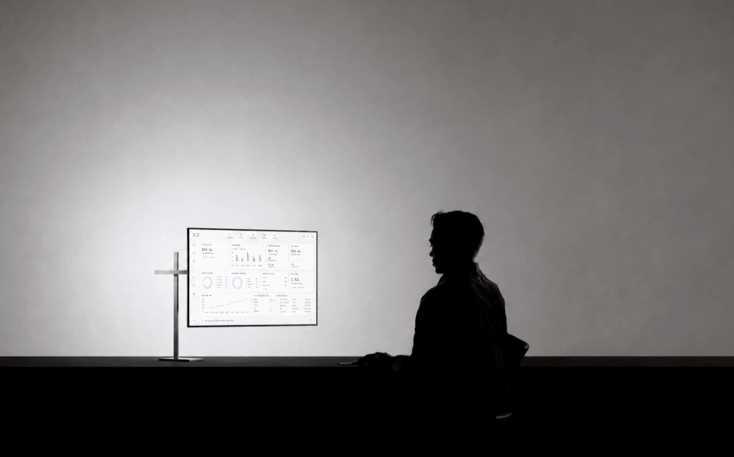 XS operator seated at a desk beside a live portfolio dashboard